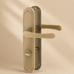 Antiek messing deurklink op ovaal langschild met toilet- en badkamersluiting